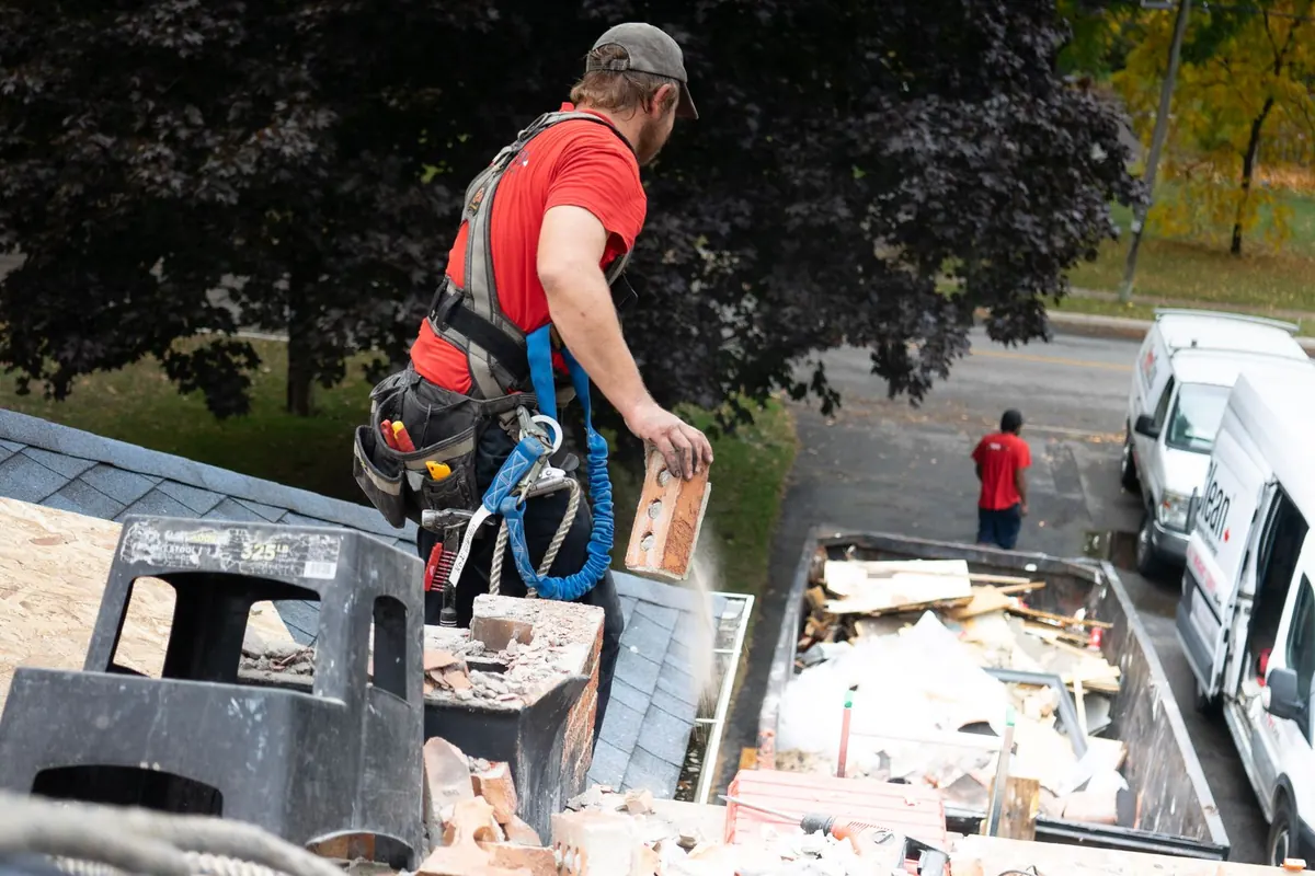 Roofing worker clearing debris from a roof into a dumpster during a tear-off